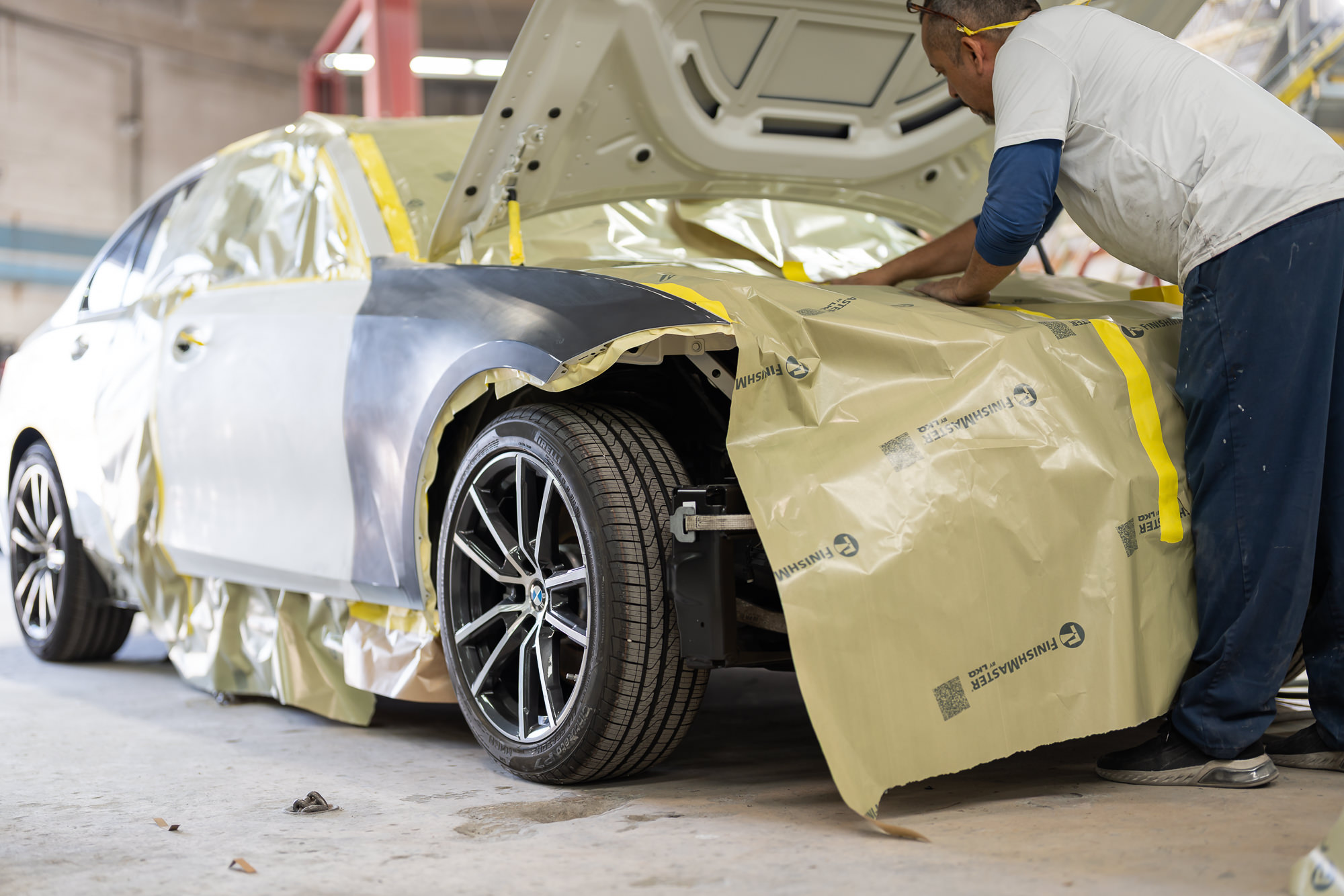 Precision technician meticulously masking a BMW before paint work