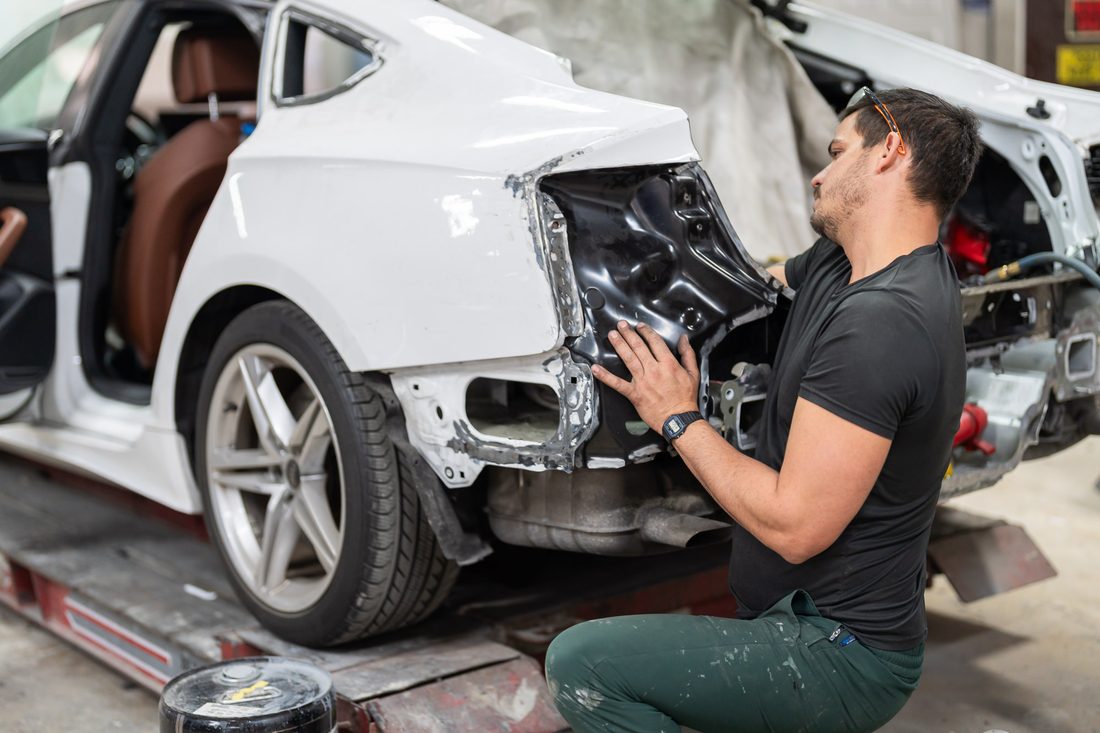 Technician test-fitting a replacement rear quarter panel on the frame rack