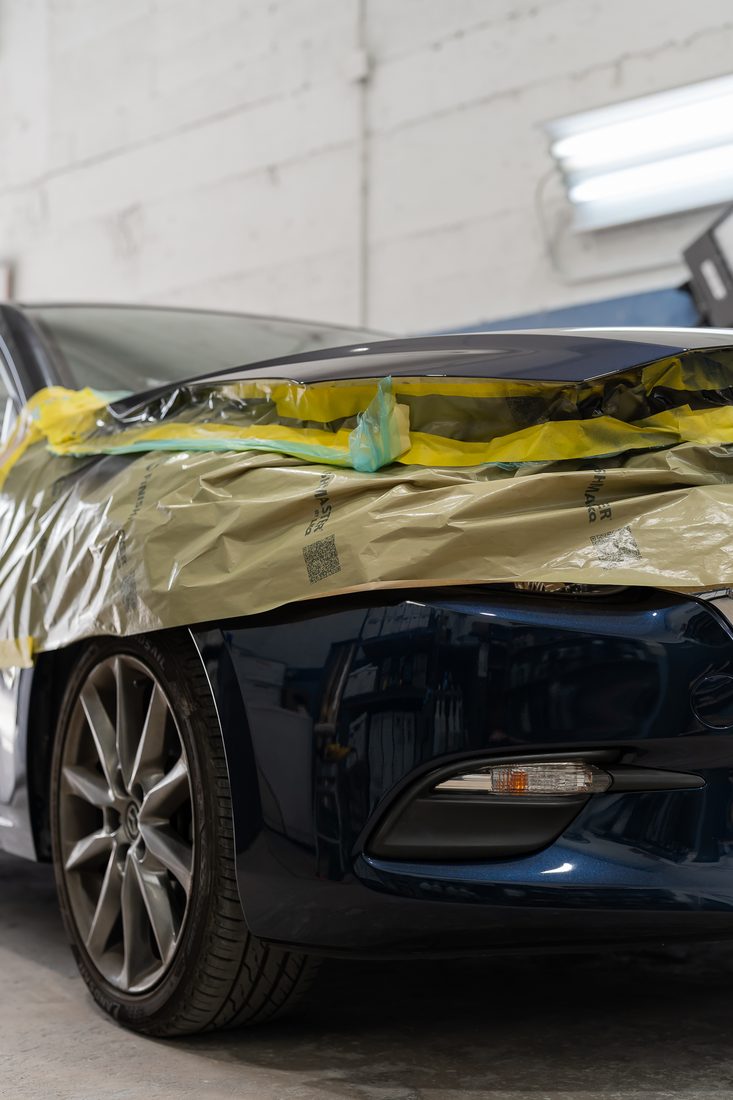 A sedan masked and taped along the front end before refinishing