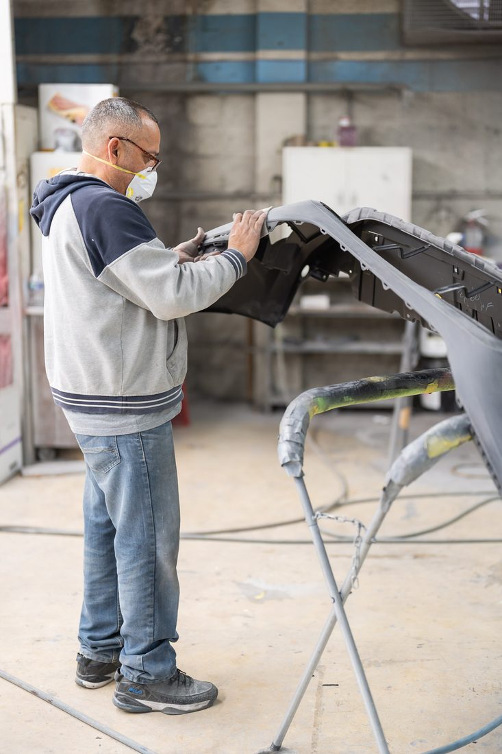 Technician in a respirator block-sanding a primed panel before paint